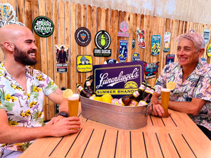 Two guys drinking craft beer in front of a giant wall of tin tackers 